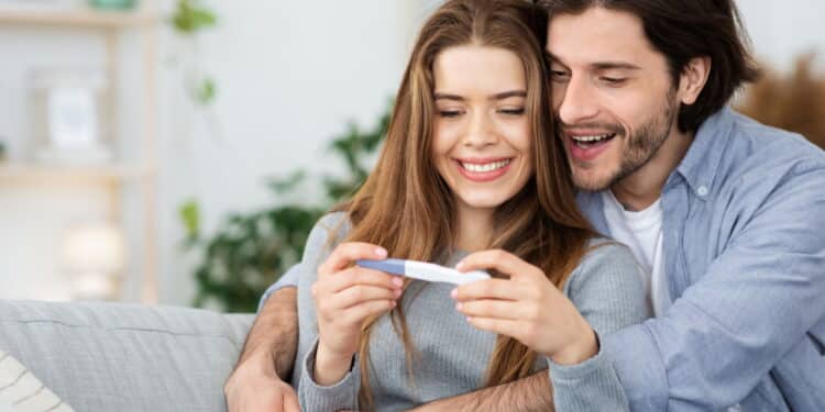 Closeup of happy hugging couple holding positive pregnancy test